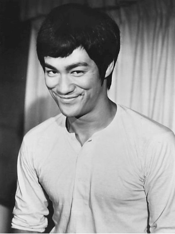 A black-and-white portrait of Bruce Lee smiling at the camera.