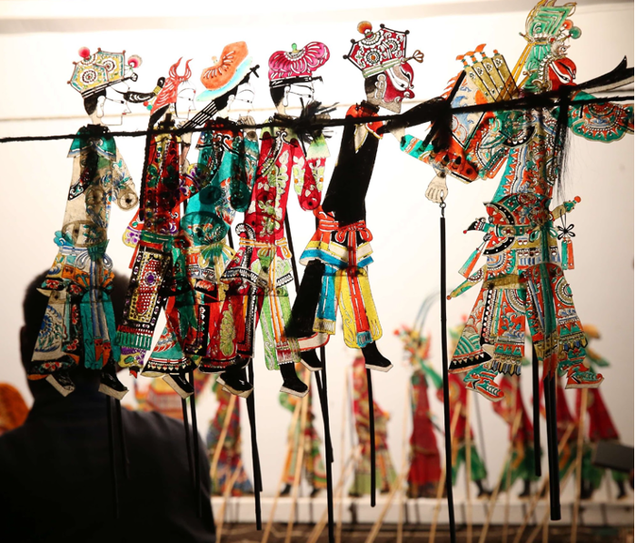 A row of colorful Chinese shadow-puppet characters mounted on control rods.